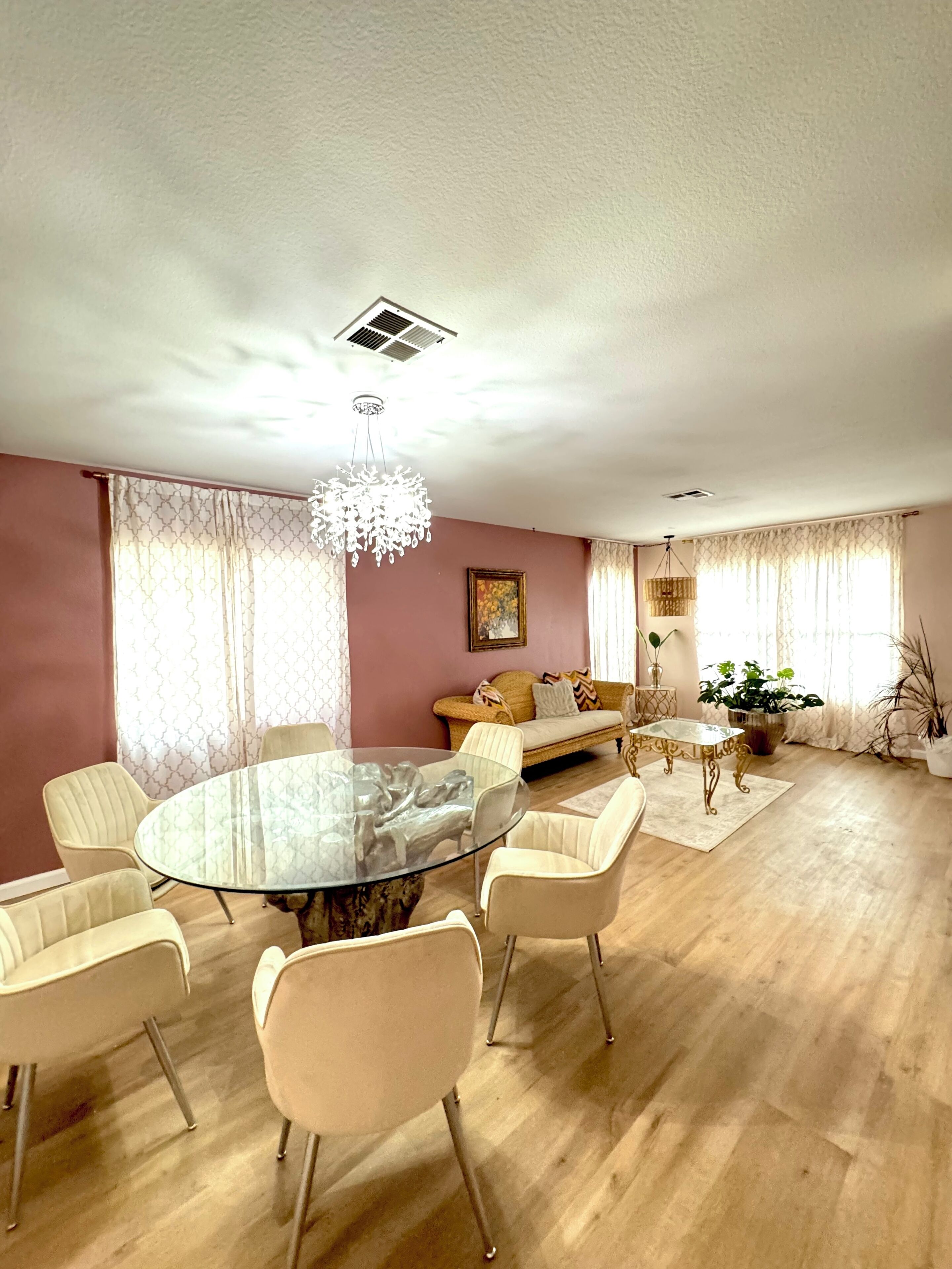 Un espace repas avec une table en verre entourée de chaises, d’un canapé et d’un lustre décoratif.