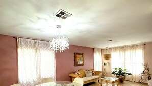 A dining area with a glass table surrounded by chairs, a sofa, and a decorative chandelier.