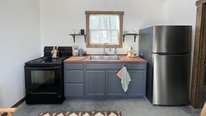 Une cuisine équipée d’une cuisinière, d’un évier et d’un réfrigérateur, avec un cadre de fenêtre en bois et un luminaire suspendu.