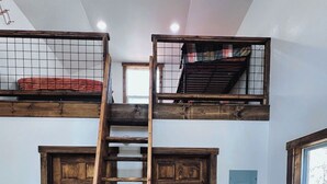 Une pièce de style « loft », avec une échelle en bois menant à un lit en mezzanine, une table à manger avec des chaises et une fenêtre offrant une vue.