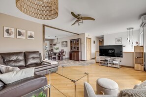 A modern living room with a leather sofa, a glass coffee table, a TV, and a dining area with a chandelier. - Maison familiale Charlesbourg, Spa (Québec)