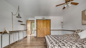 Een slaapkamer met een houten garderobe, een bed met een bedeksel met patroon, een plafondventilator en een gang naar een badkamer.