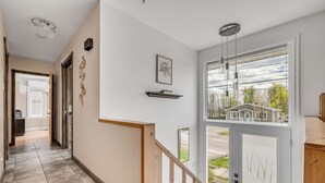 Een gang met een houten trap, een deur met uitzicht op huizen, en een plafondlamp.