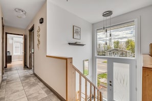 A hallway with a wooden staircase, a door with a view of houses, and a ceiling light fixture. - Maison familiale Charlesbourg, Spa (Québec)