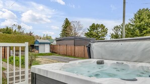Een hottub met een houten terras, een wit hek en een kleine schuur in een achtertuin.