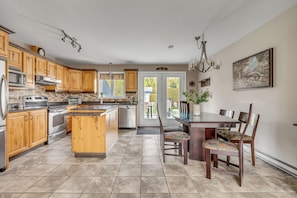 A kitchen with wooden cabinets, stainless steel appliances, a dining table with chairs, and a view through a glass door. - Maison familiale Charlesbourg, Spa (Québec)
