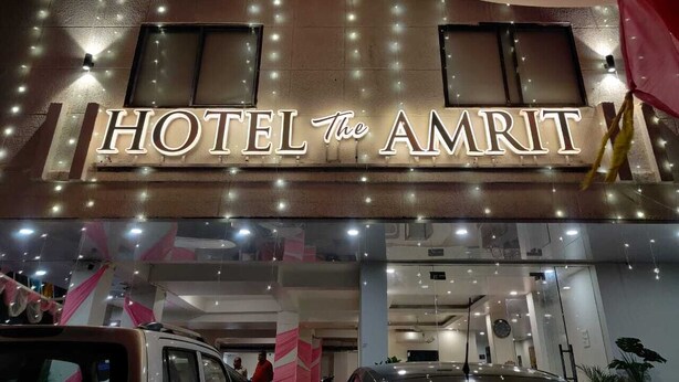 Et hotelskilt med navnet 'HOTEL The AMRIT' og et moderne interiør med synlige vinduer og loftslamper.