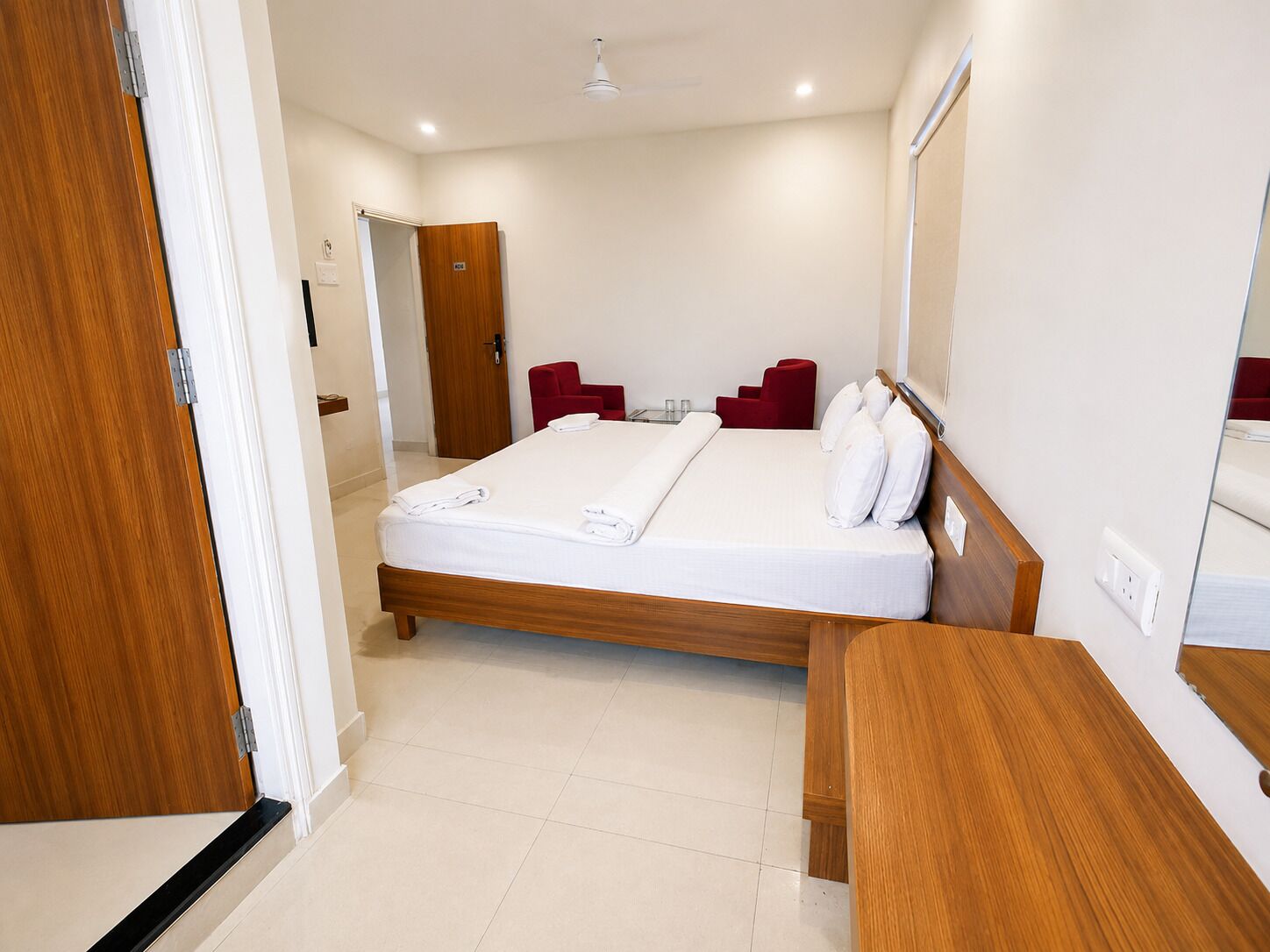 A hotel room with a wooden bed, a bedside table, a red chair, and a mirror on the wall.