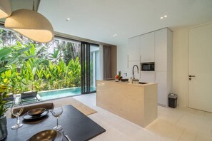 A modern kitchen with a built-in microwave, a small sink, and a dining area with a table set for two. - Garden Village 4 (Ubud)