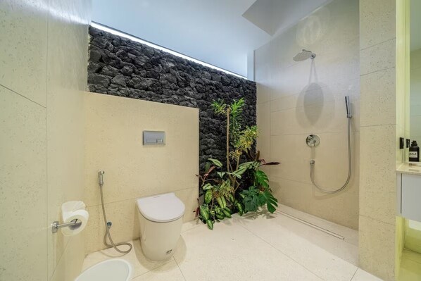 Ein modernes Badezimmer mit einer Wand aus Stein, einer Toilette, einem Bidet und einer Dusche.