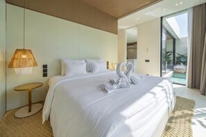 Ein modernes Hotelzimmer mit einem großen Bett, einem runden Tisch, einer Wandlampe und Blick auf einen Swimmingpool.