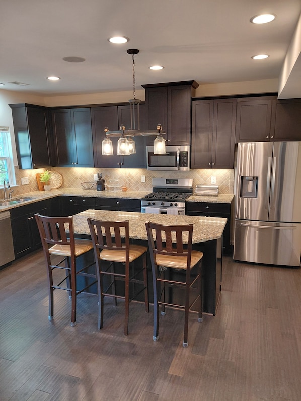 A modern kitchen with dark cabinets, stainless steel appliances, and a central island with bar stools.