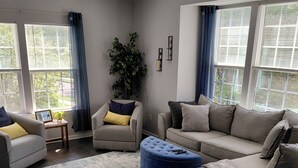 Un salon avec une grande fenêtre, une plante en pot et un tapis bleu et blanc.