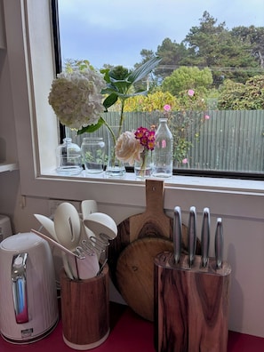 Una encimera de cocina con vista al exterior, una tabla de cortar de madera, un portalapieles y un escurreplatos.