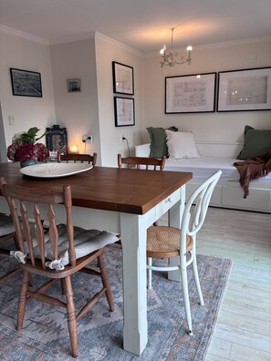 En matplats med ett träbord och stolar, en matta och en vit soffa i bakgrunden.