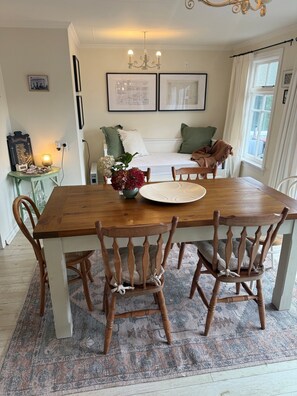 Un comedor con una mesa de madera, sillas, un jarrón de flores y una araña.
