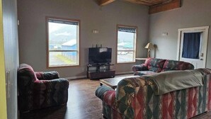 Una sala de estar con dos sofás estampados, un televisor sobre un mueble bajo y grandes ventanales con vistas.