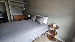 Un dormitorio con cama, cómoda, lámpara y una mesita redonda.