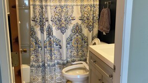 Un baño con cortina de ducha estampada, un inodoro, un lavabo y una toalla colgada en la pared.