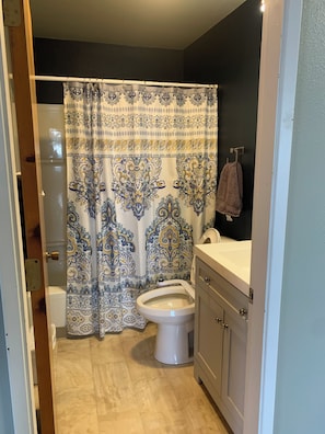 Une salle de bain avec un rideau de douche à motifs, des toilettes, un lavabo et une serviette accrochée au mur.