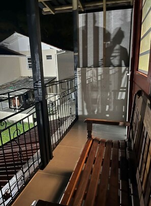 Ein Balkon mit Metallgeländer, einer Holzbank und Blick auf ein Gebäude im Hintergrund.