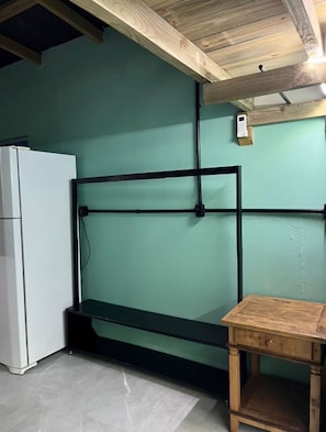 Ein Zimmer mit einem weißen Kühlschrank, einem schwarzen Metallregal und einem Holztisch.