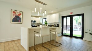 A modern kitchen with white cabinets, stainless steel appliances, and a bar area with two white bar stools. - World Cup Oasis. 12 min from Beach & Casino. 18 min from World Cup stadium. (Hollywood)