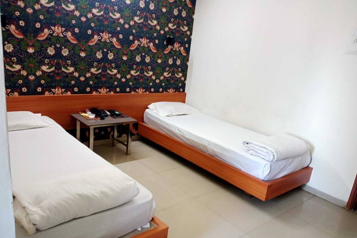Una habitación con dos camas individuales, una mesita y un papel tapiz estampado.