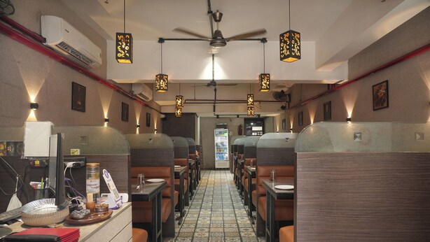 Un restaurante con cabinas, suelo de baldosas, luces colgantes y un ventilador de techo.