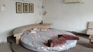 Un dormitorio con una cama curvada, un ventilador de techo, un equipo de aire acondicionado y cuadros en la pared.