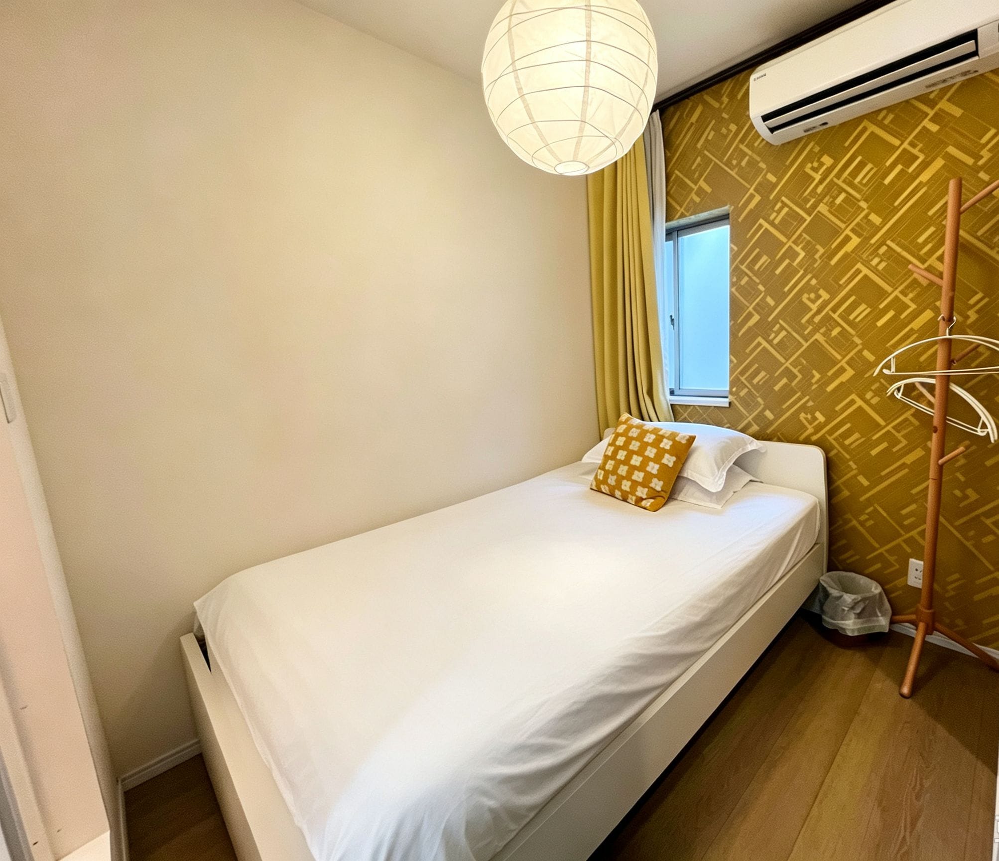 A single bed with white bedding, a hanging light fixture, an air conditioning unit, and a patterned wall.