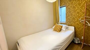 A single bed with white bedding, a hanging light fixture, an air conditioning unit, and a patterned wall.