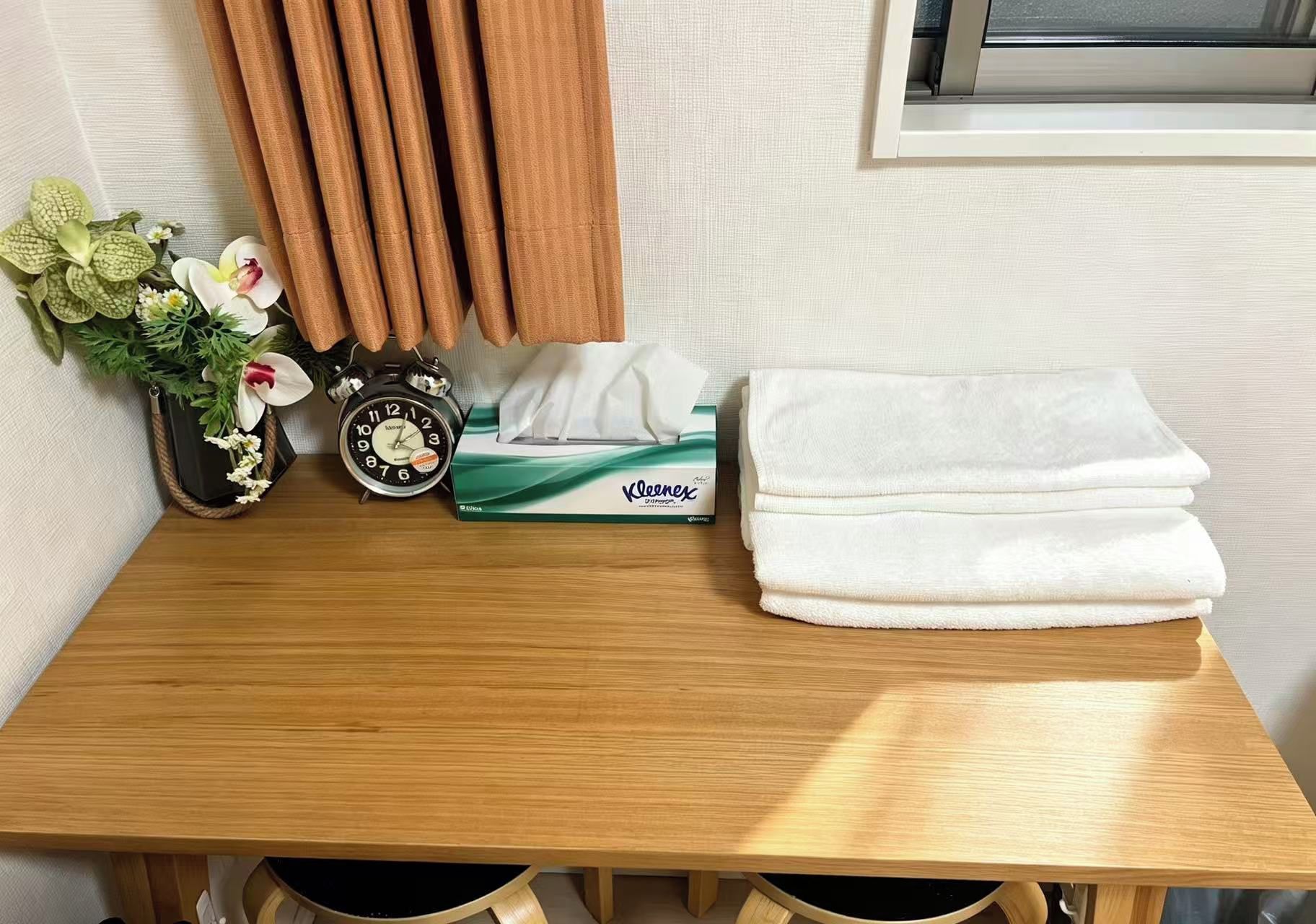 Ein Holztisch mit einer Taschentuchbox, einem gefalteten weißen Handtuch und einer Uhr mit Blumen.