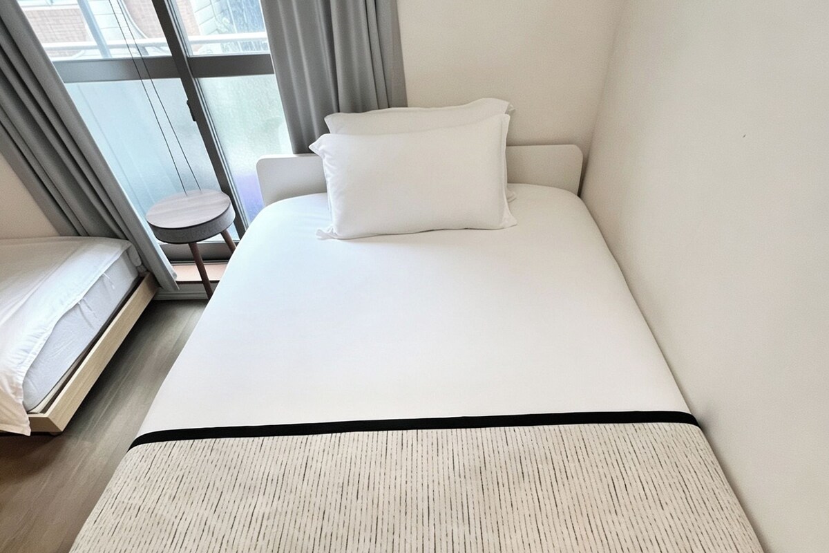 A hotel room with a bed, a small table, and a window with curtains.