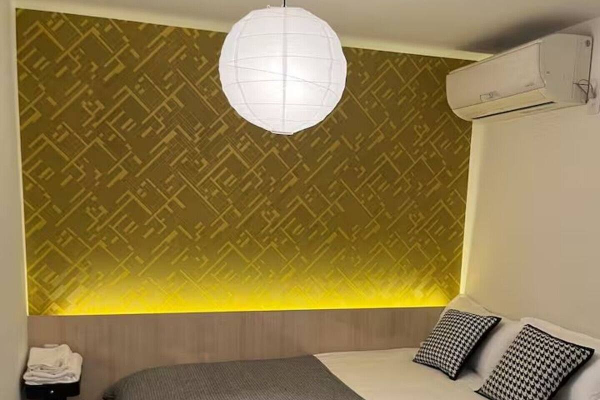 Quarto com cama, luminária pendente, aparelho de ar condicionado e parede estampada.