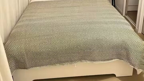 Un lit avec une couvre-lit à motifs, deux oreillers à carreaux et une table de chevet sur laquelle est posée une plante.