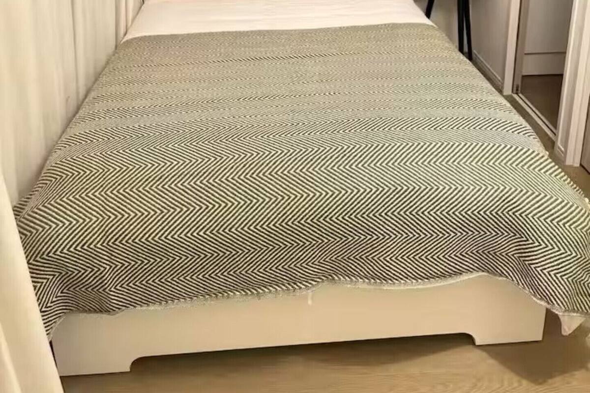 Uma cama com colcha estampada, duas almofadas com padrão xadrez e uma mesa de cabeceira com uma planta.