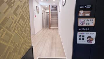 A hotel corridor with a wooden floor, a staircase, and various signs including a no-smoking sign and a sign requesting silence.