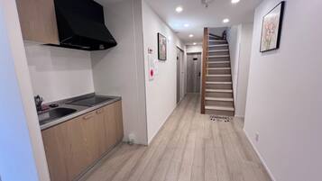 A modern kitchen with a built-in stove, wooden cabinets, and a black range hood. A hallway with a wooden staircase leads to another room.