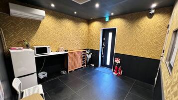 A room with a microwave, a small table, a chair, a fire extinguisher, and a door with a sign.