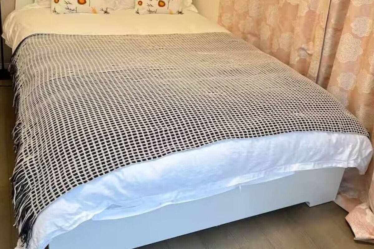 Uma cama com colcha de padrão preto e branco, cabeceira com desenho geométrico e uma parede com cortina estampada.