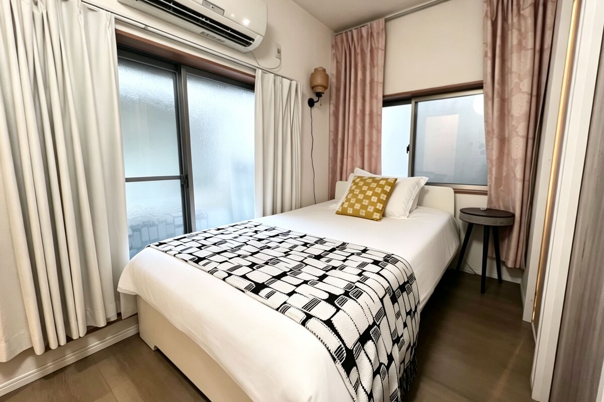 A hotel room with a bed, a small table, and an air conditioning unit.