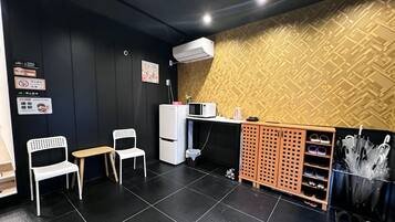 A modern interior with a black and gold patterned wall, a white refrigerator, a microwave, a small table, two white chairs, and a shoe rack.