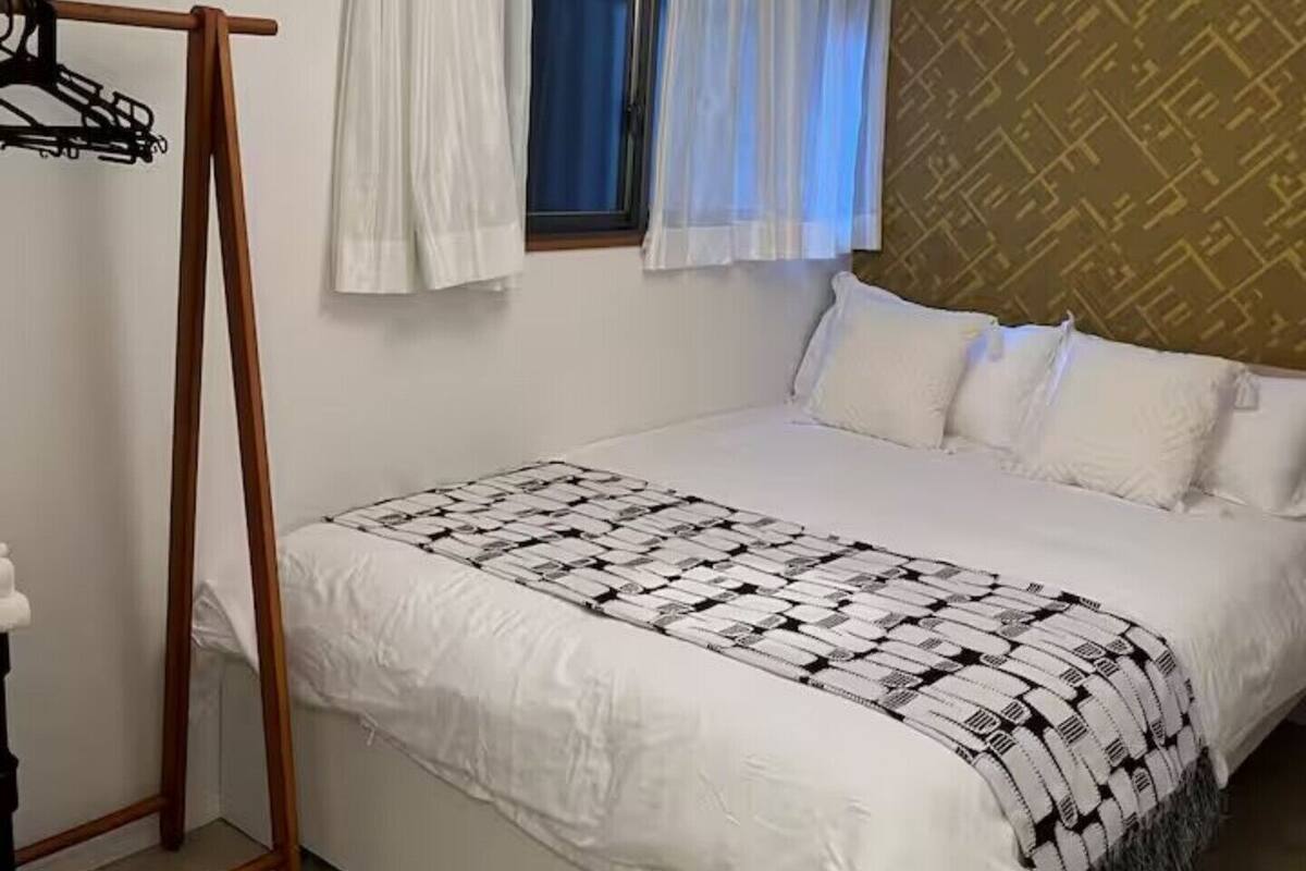 Quarto com cama, janela com cortinas, luminária pendente e parede com padrão geométrico.