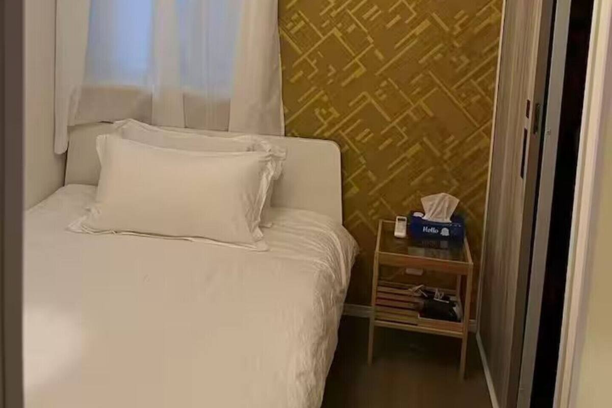 Quarto de hotel com uma cama, ar condicionado, uma pequena mesa e uma caixa de lenços, além de uma parede estampada.