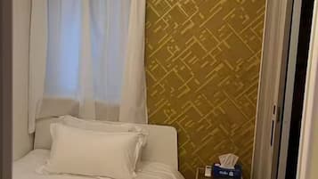 Une chambre d’hôtel avec un lit, un climatiseur, une petite table avec une boîte de mouchoirs et un mur décoré d’un motif.