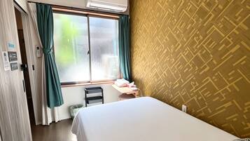 A hotel room with a bed, a window with curtains, an air conditioning unit, a wall with a geometric pattern, and a door with a towel rack.