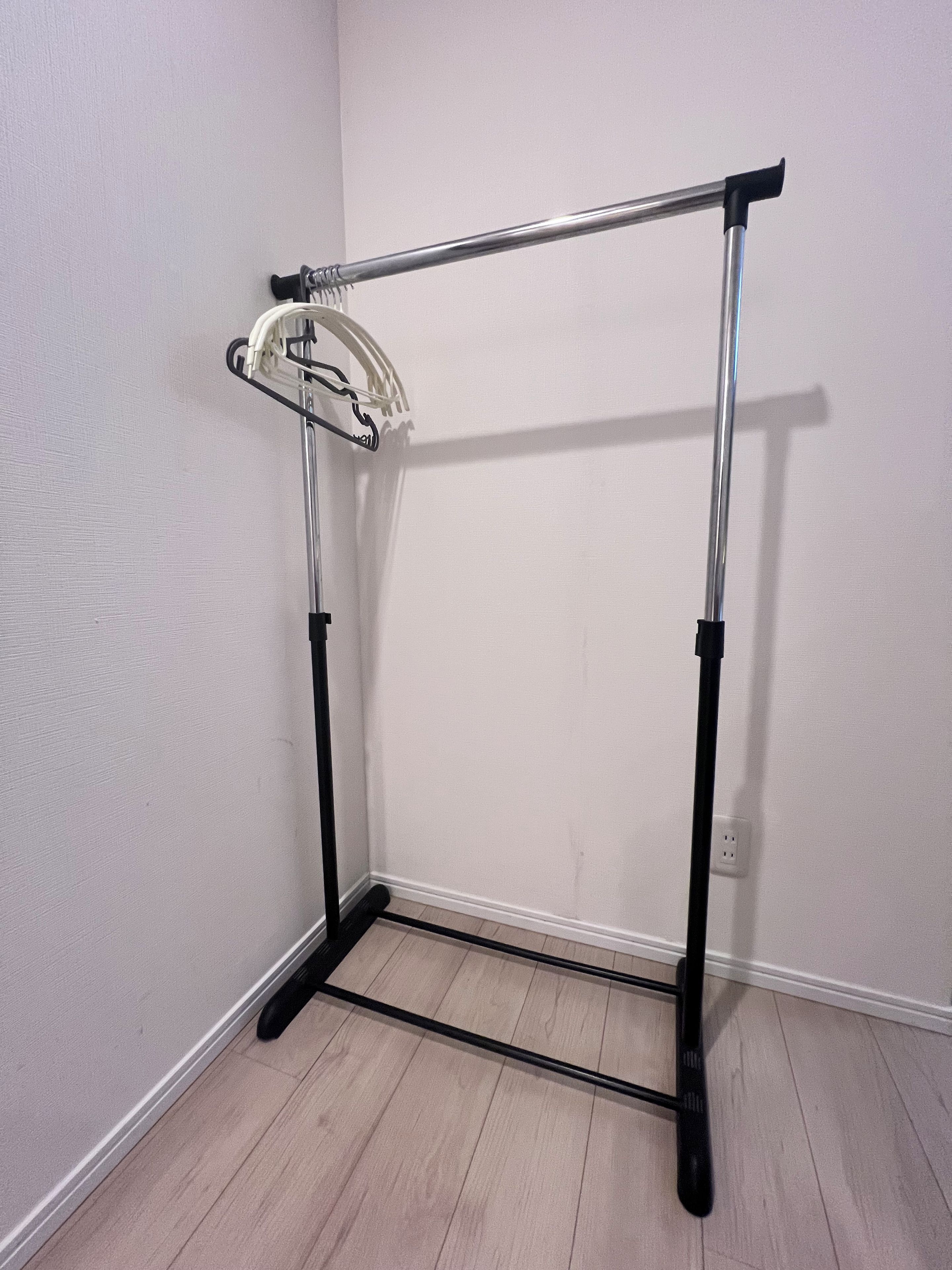 A corner room with a metal rack against the wall, a white floor, and a visible electrical outlet.