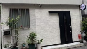 Un bâtiment moderne à deux étages, doté d’une porte noire, de plantes en pot et d’une caméra de surveillance.