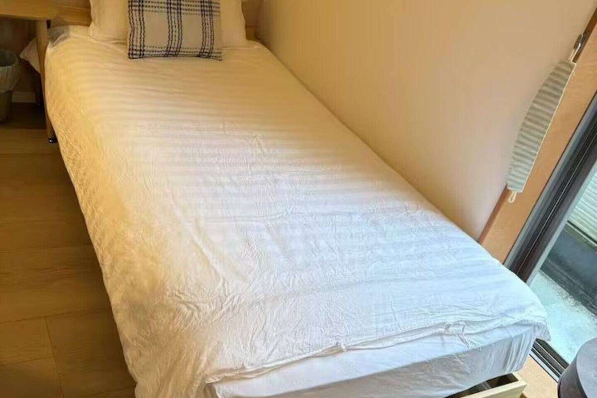 Uma cama de solteiro com estrutura de madeira, encosto e travesseiro xadrez.